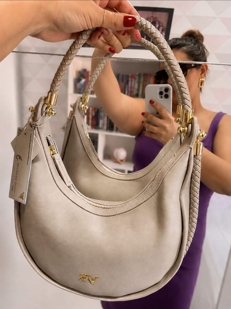 Giselle segurando a Bolsa Meia Lua Pavão de Ouro em frente ao espelho